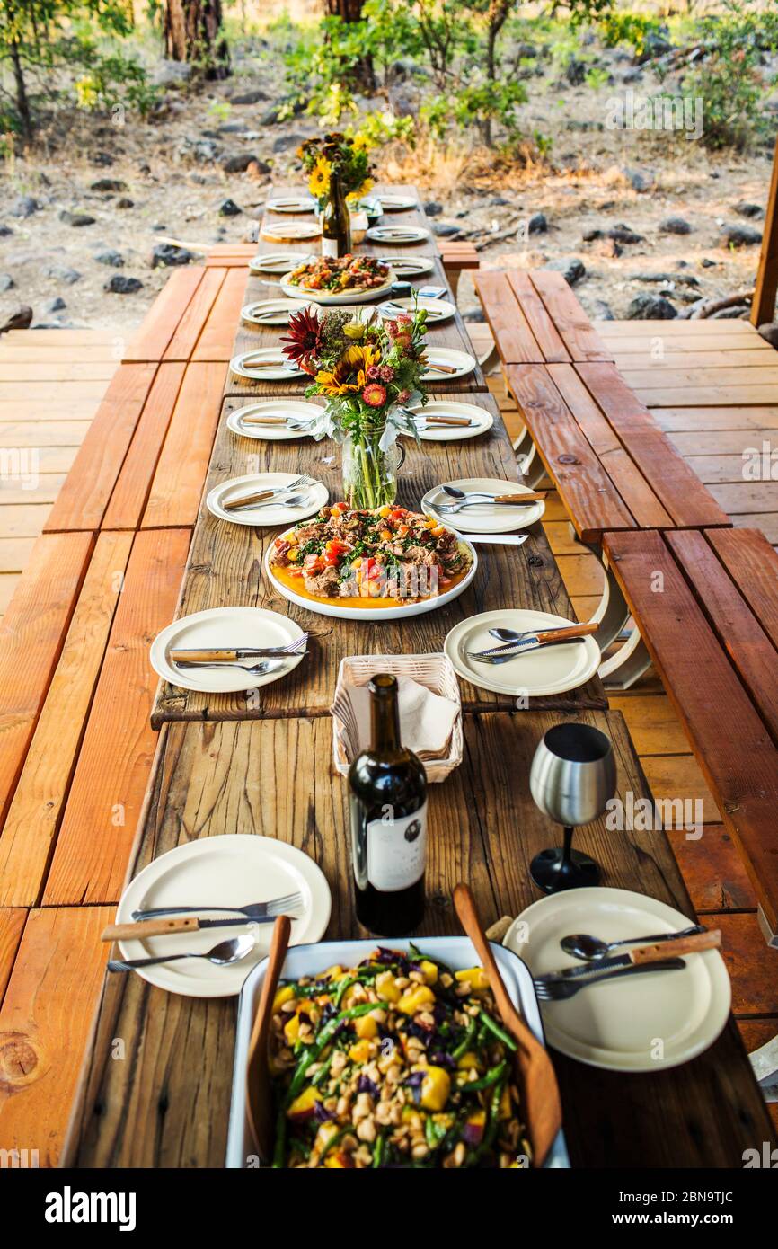 A long wooden table set for dinner in open-air setting Stock Photo