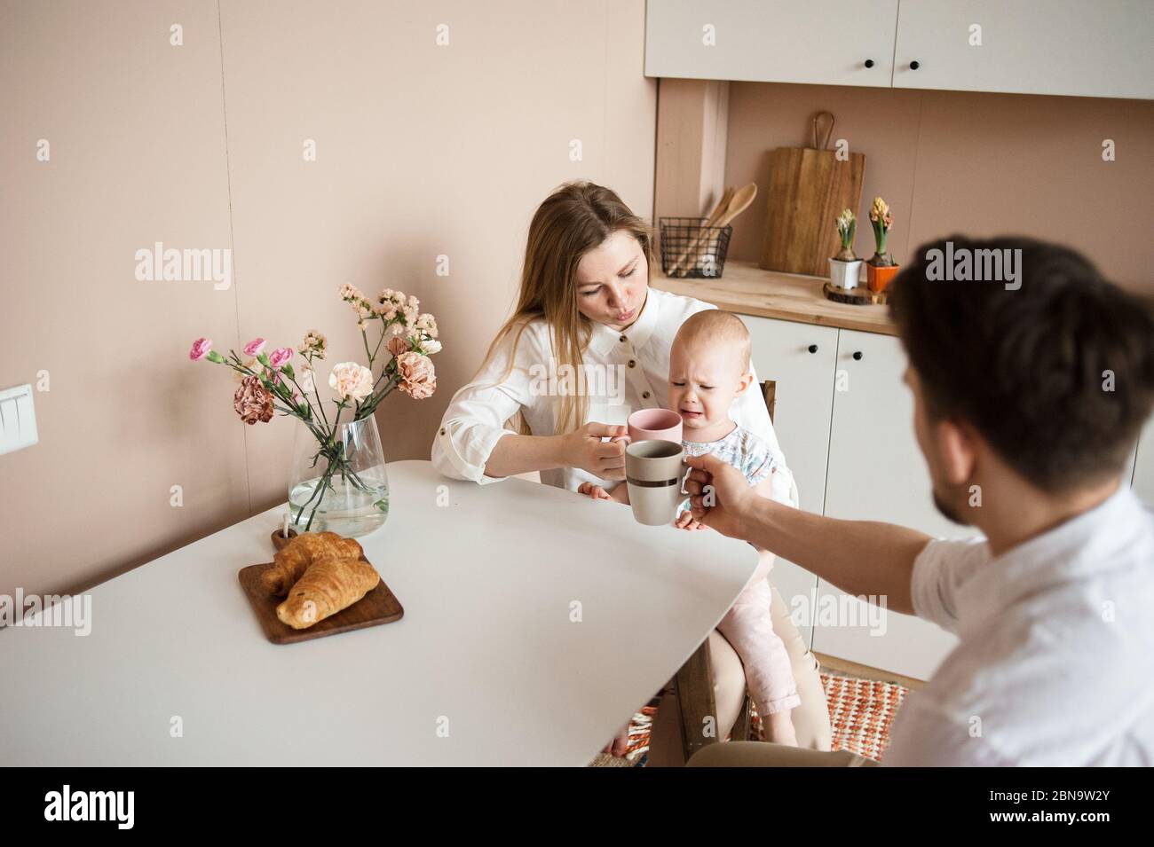 Parents comfort a crying child in the modern kitchen. Family routines Stock Photo