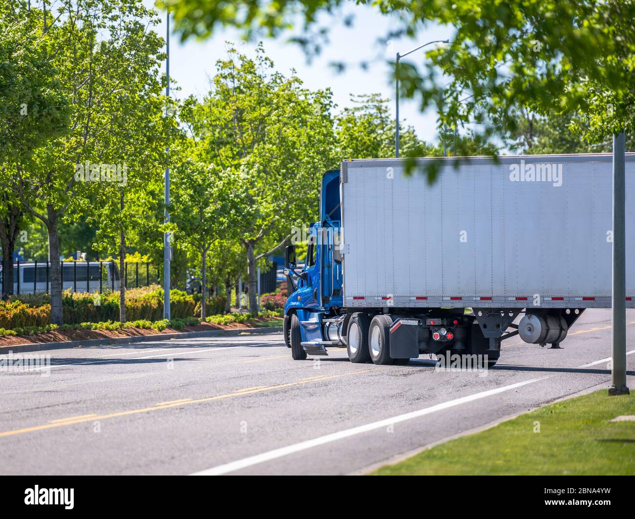 Blue day cab industrial diesel big rig semi truck with roof spoiler for reduce air resistance and improve aerodynamics transporting cargo in dry van s Stock Photo