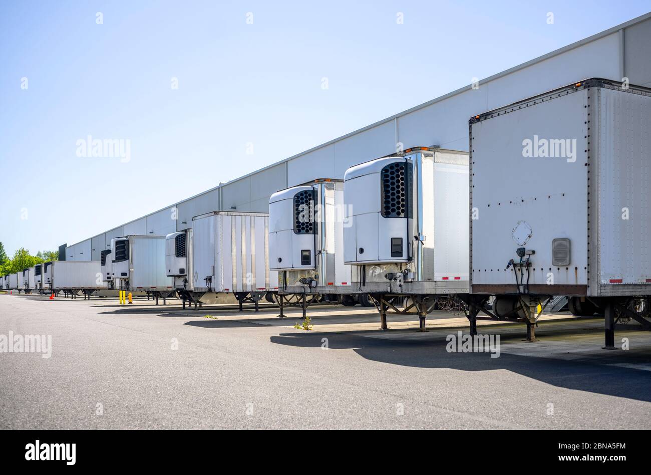 Industrial grade refrigerator and dry van semi trailers with reefer units on the front wall and without it standing at warehouse dock gates loading co Stock Photo