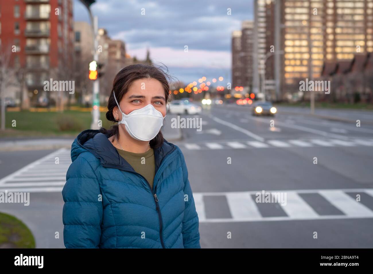 Covid-19 pandemic coronavirus concept. Young beautiful woman in protective medical face mask standing on street by the road. Stock Photo