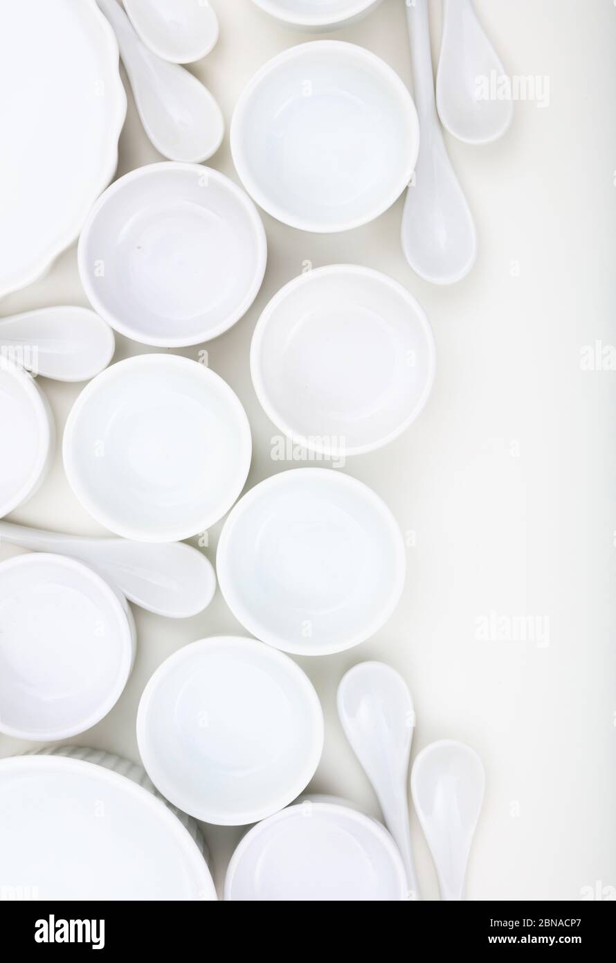 Dishware concept. White empty porcelain bowls and teaspoons background. Clean, new, luxury soup pots and spoons, vertical photo. Stock Photo