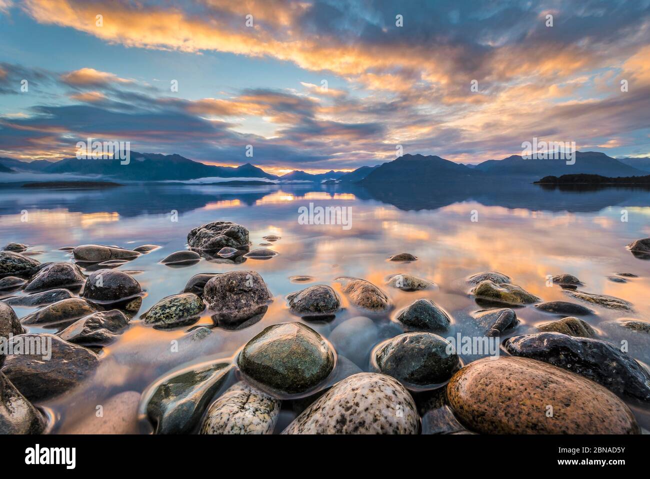 Light beam of golden cloud atmosphere over Lake Te Anau, in the back mountain ranges of the Stuart Mountains and Franklin Mountains, in the front roun Stock Photo