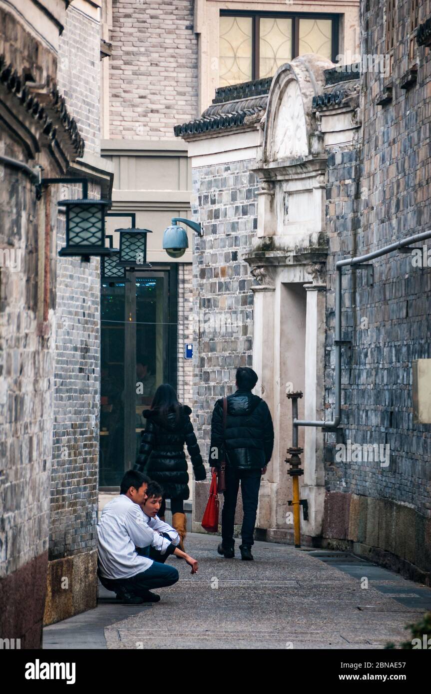 Two chefs have a break and a smoke as a couple pass by in Ningbo's Moon Lake Flourishing Garden area of restaurants and bars Stock Photo