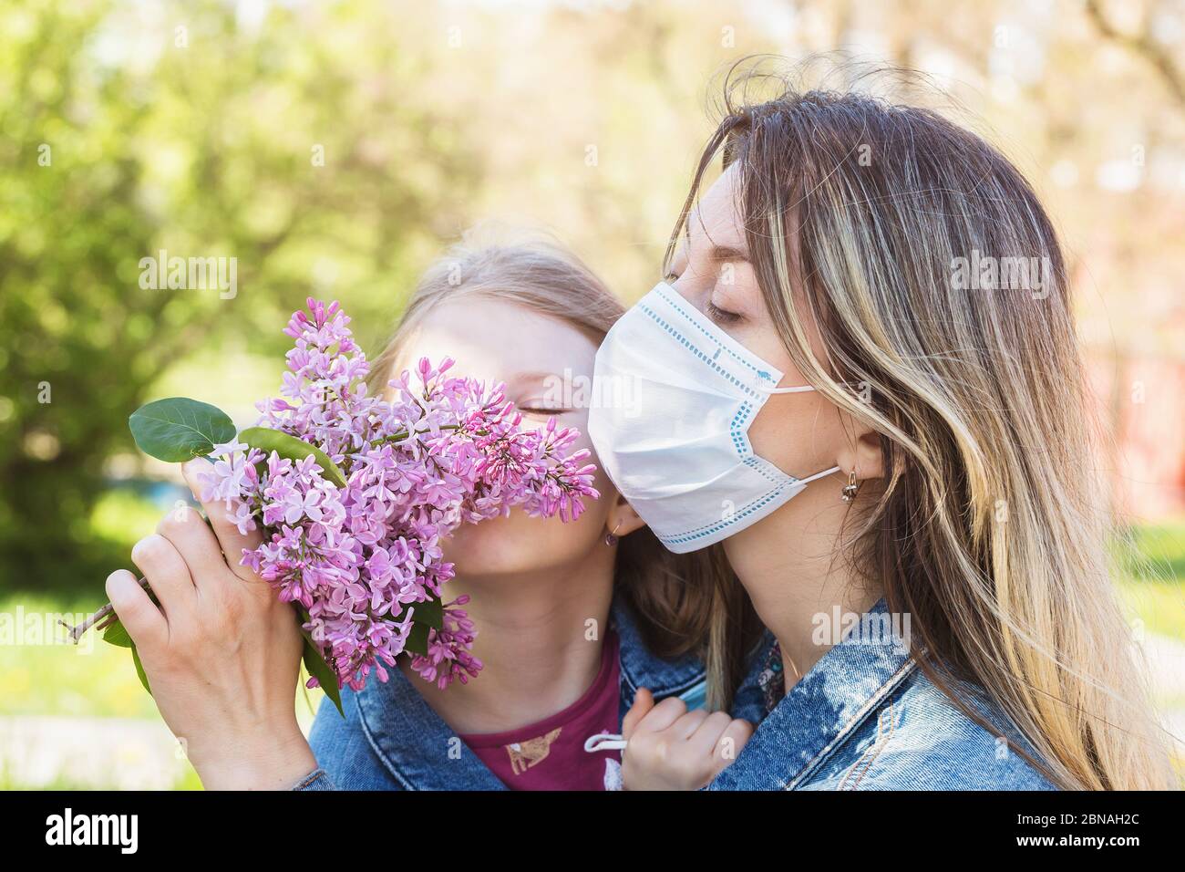 Mom and daughter sniffing a lilac on the street. Quarantine quit concept Stock Photo