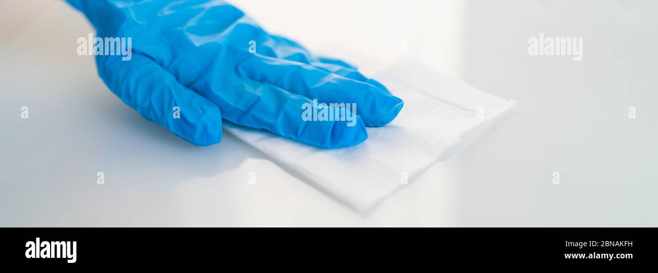 Surface cleaning against spreading of coronavirus person wearing gloves with antibacterial disinfecting wipe wiping glass table. banner panoramic background. Stock Photo