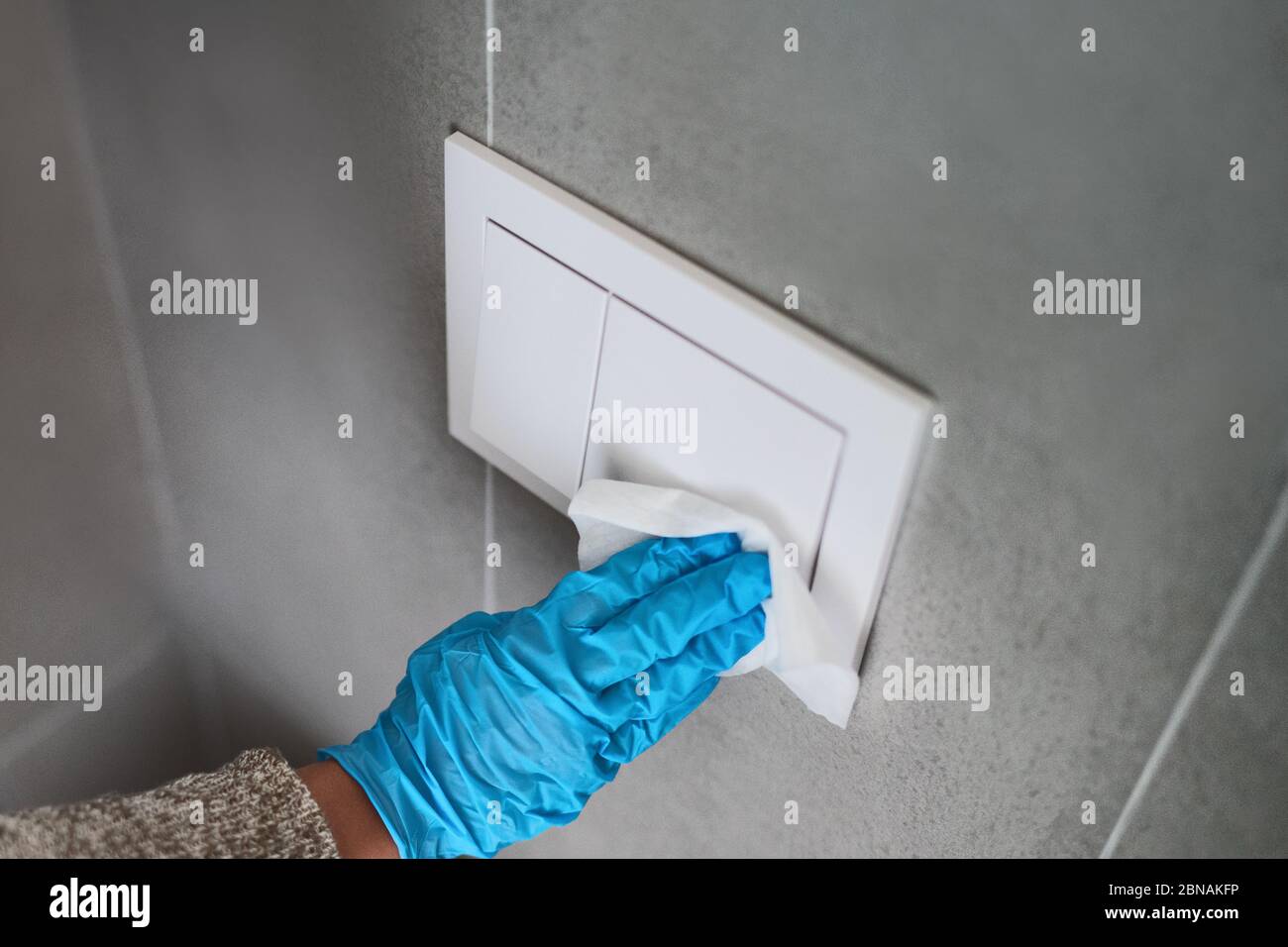 Surface sanitizing wipes of home surfaces, wall button switches wiping paper towel sanitizer with gloves. Stock Photo