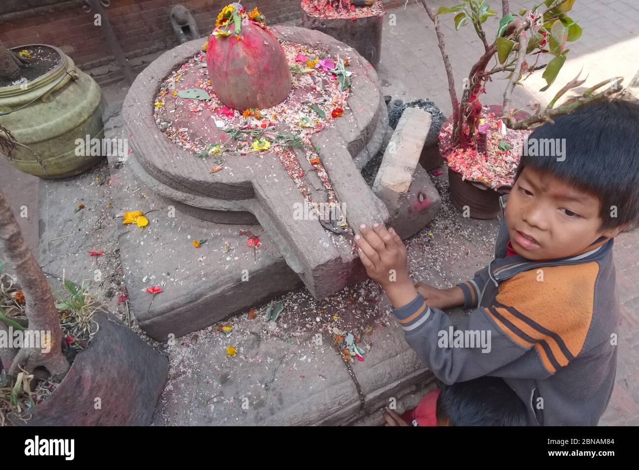 A Nepalese boy poses next to a Lingam inside a Yoni, symbols for Hindu god Shiva & goddess Shakti respectively; Bhaktapur, Kathmandu Valley, Nepal Stock Photo