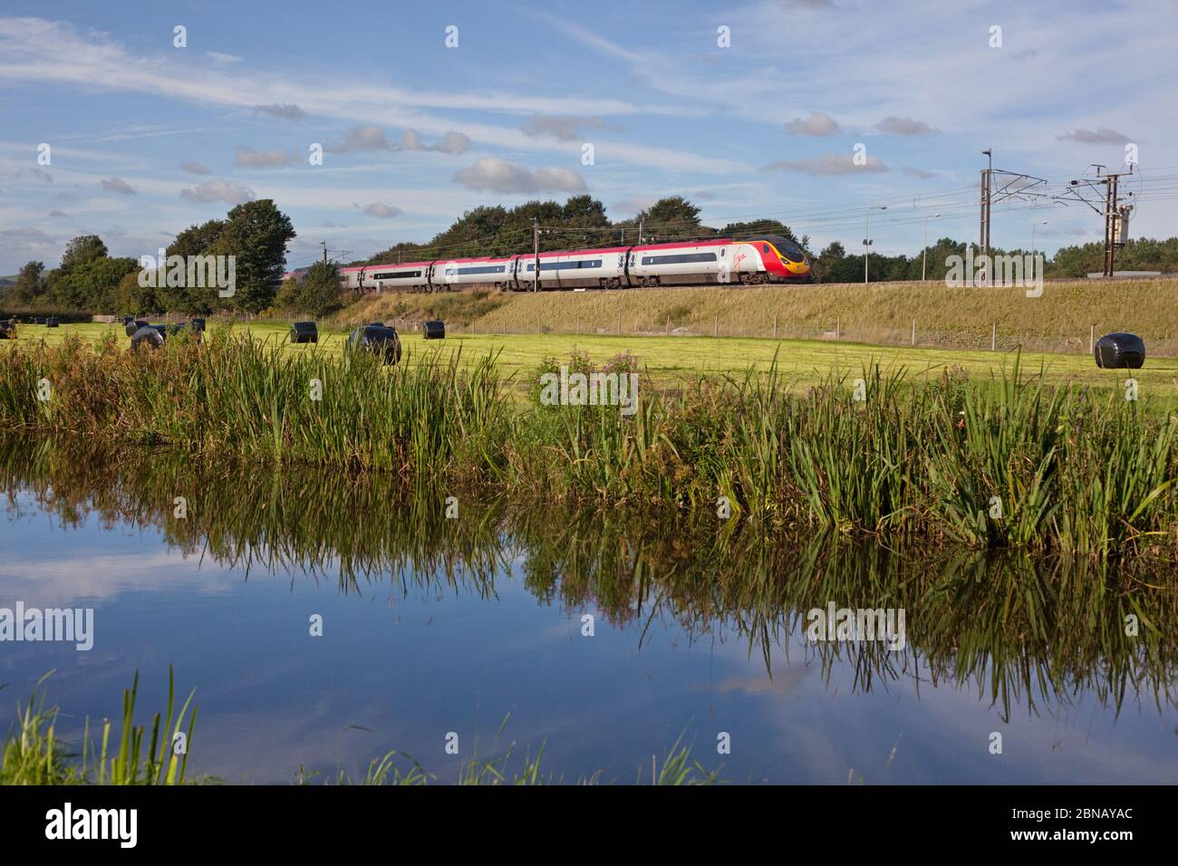 Virgin trains Alstom Pendolino train on the electrified west coast mainline in the countryside by the canal at  Catterall, Lancashire Stock Photo