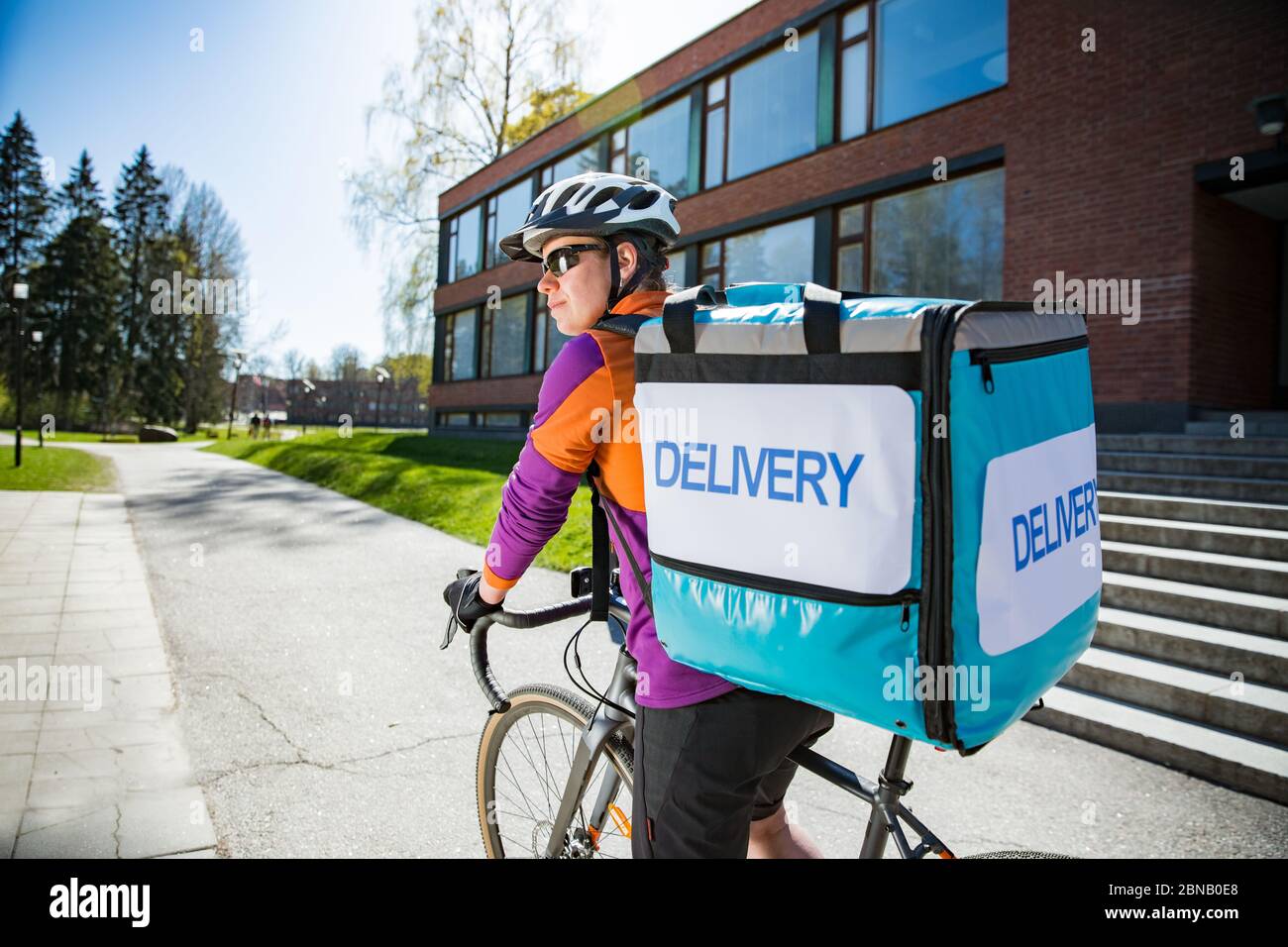 Woman in helmet with big food delivery backpack riding bike on the street.  Sunny spring day in the city. Portrait of a female courier on a Bicycle  Stock Photo - Alamy