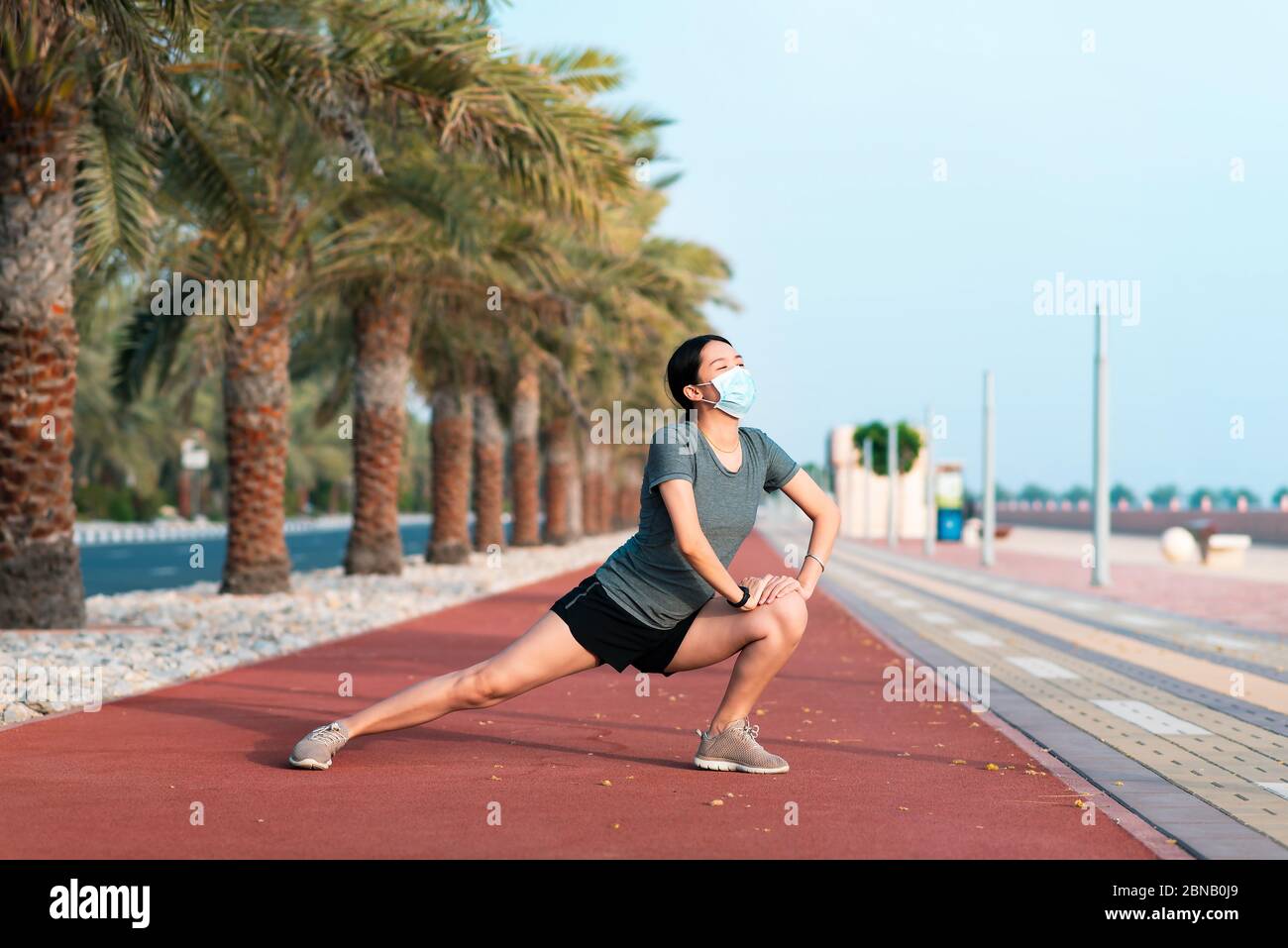Asian woman exercising and stretching while wearing protective surgical mask to warm up before fitness workout outdoors Stock Photo