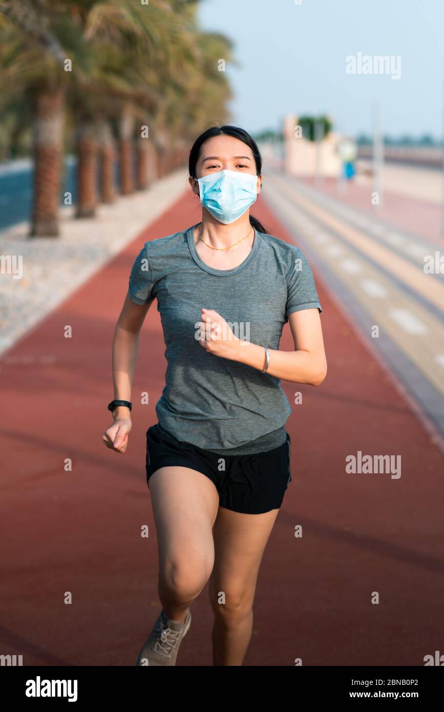 Asian woman jogging on the running track wearing protective surgical mask to prevent coronavirus spreading and stay safe Stock Photo