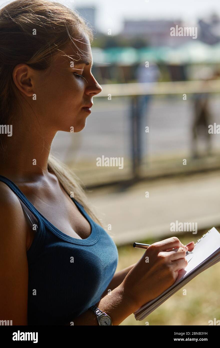 Young beautiful girl writes something in her notebook while standing in the park. Stock Photo