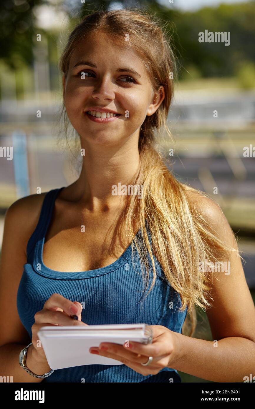 Young beautiful girl writes something in her notebook while standing in the park. Stock Photo