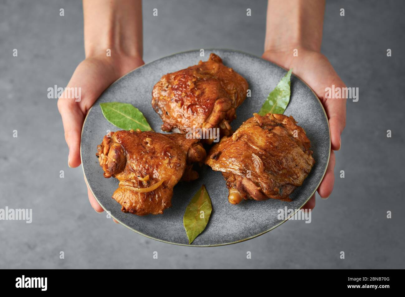 Filipino Chicken Adobo on gray plate in female hands. Chicken Adobo is