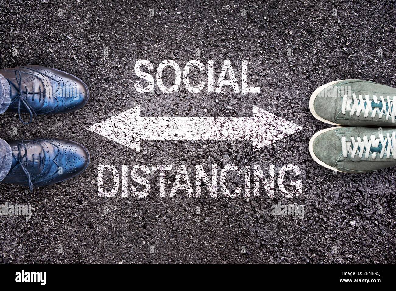 Two pair of shoes separated with message 'Social distancing' written on asphalt ground Stock Photo