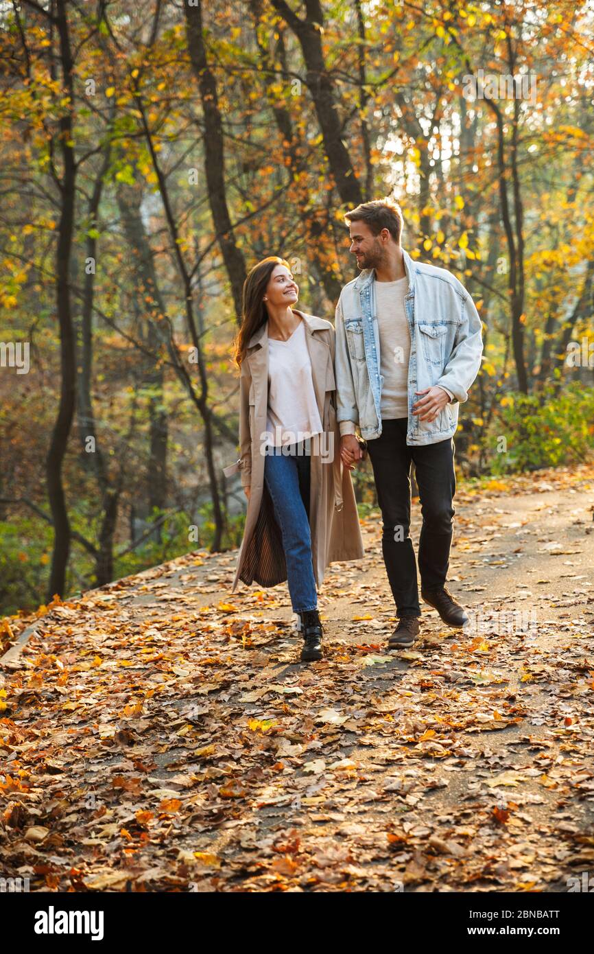 Full length of a beautiful young couple in love walking at the autumn park, holding hands Stock Photo