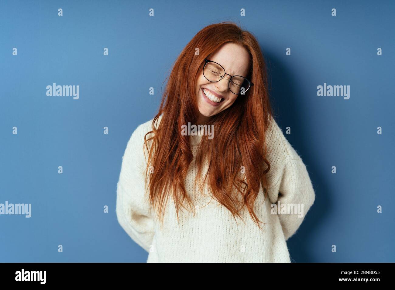 Cute young redhead woman with a lovely smile screwing up her eyes as she  grins happily at the camera on a blue studio background with copy space  Stock Photo - Alamy