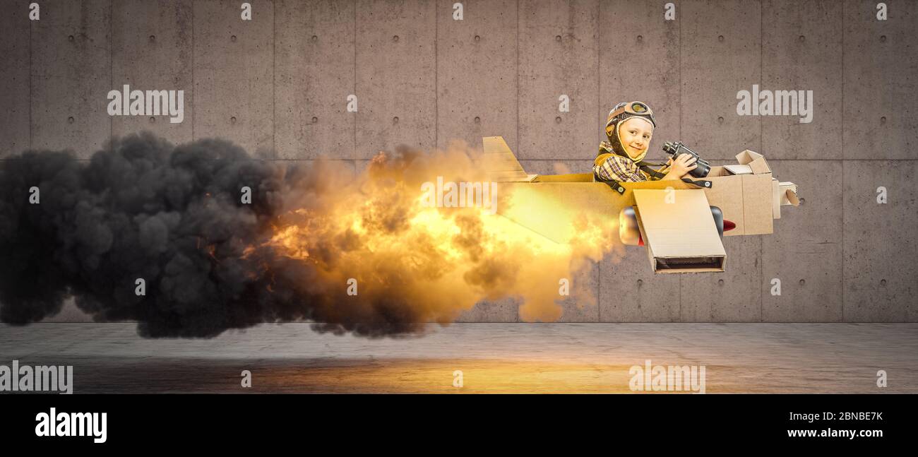 little boy plays to be an aviator on a cardboard plane, flames and smoke from the back. Face happy and smiling. concept of light-heartedness, aspirati Stock Photo