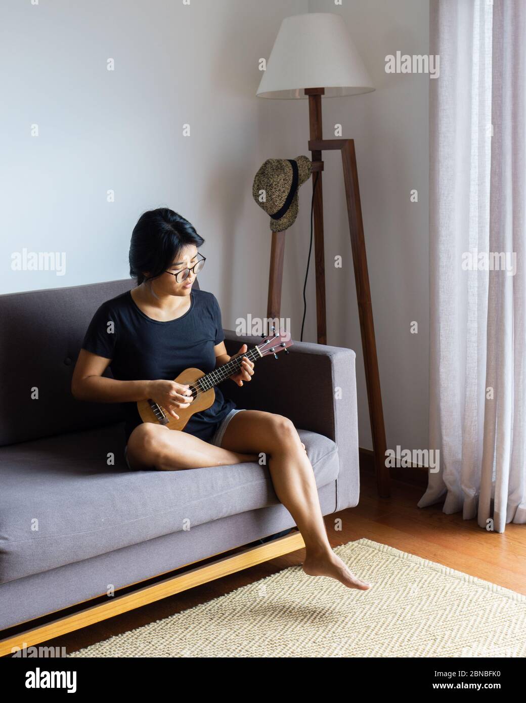 Young women playing the ukulele inside a home on a couch in the living room Stock Photo