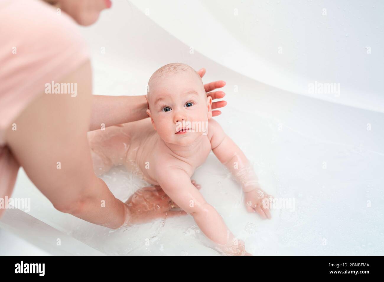 Mother's hands washing a baby. A baby boy bathes in a bath. Caring