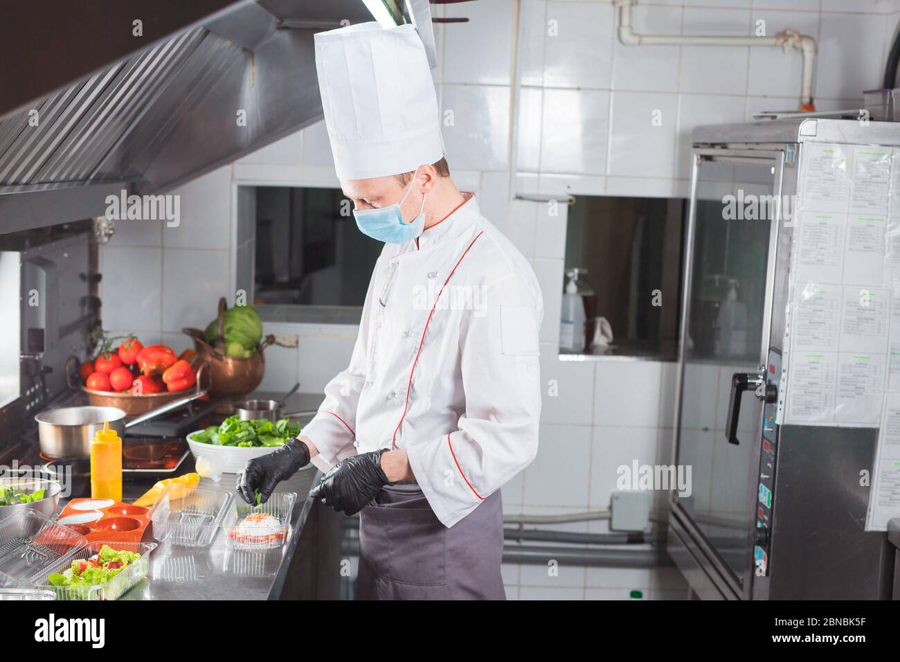 Cooking in a restaurant by a cook in a medical mask and packing in a container Stock Photo