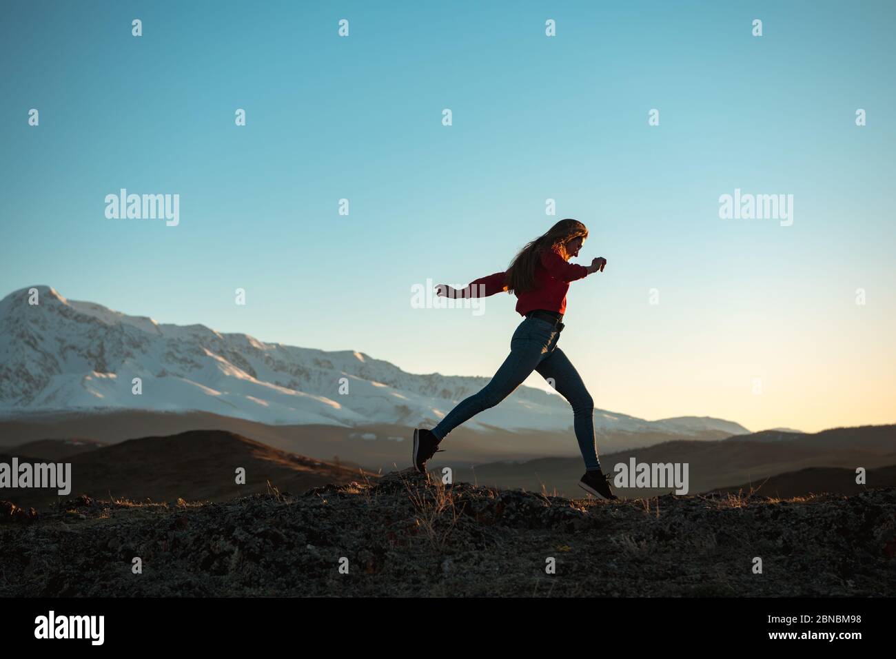 Slim sporty girl is walking in mountains at sunset time Stock Photo