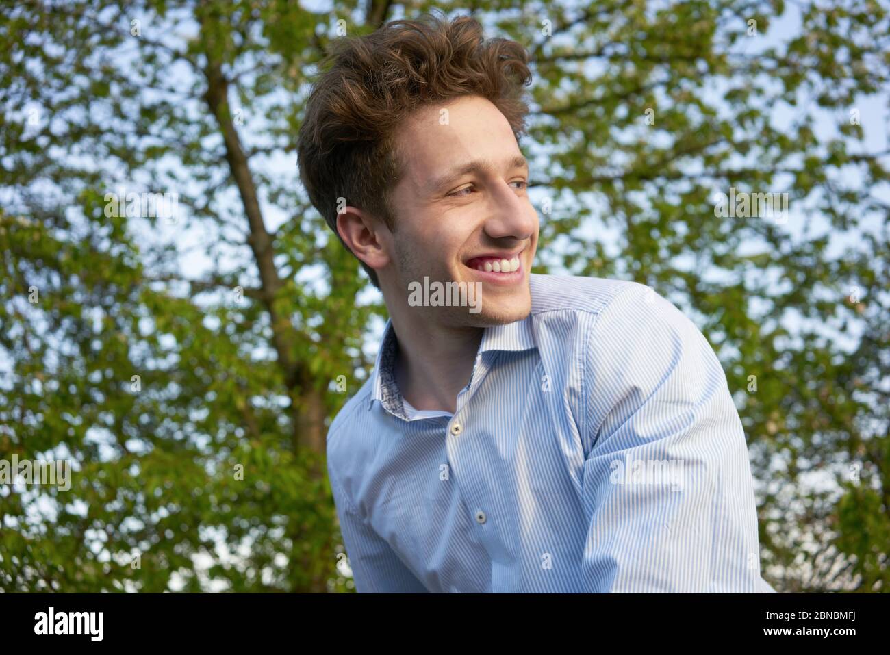 Portrait of a young handsome happily laughing man looking over his shoulder in beautiful greenery Stock Photo