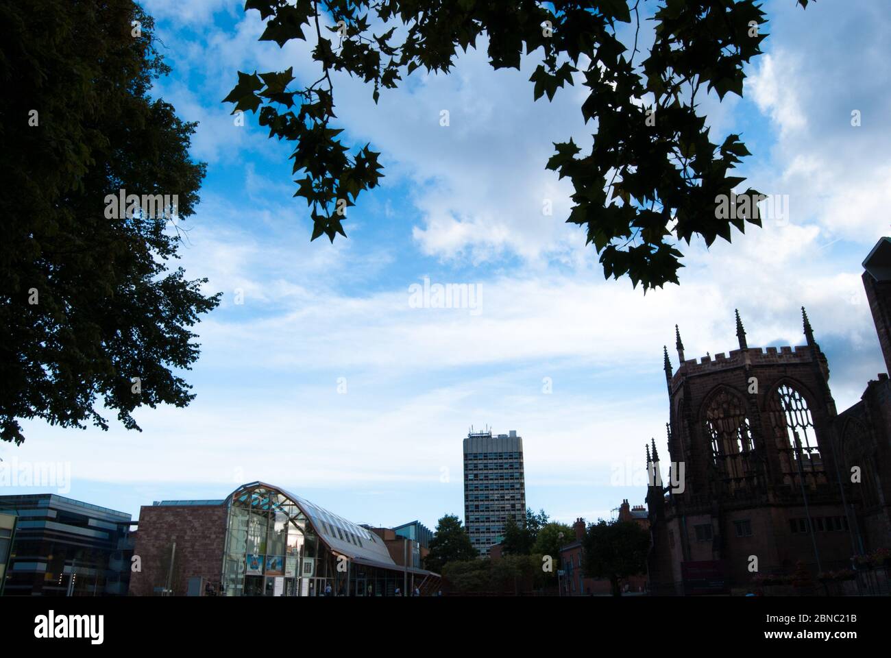 Coventry Cathedral surrounded by buildings and trees under a cloudy sky in England Stock Photo