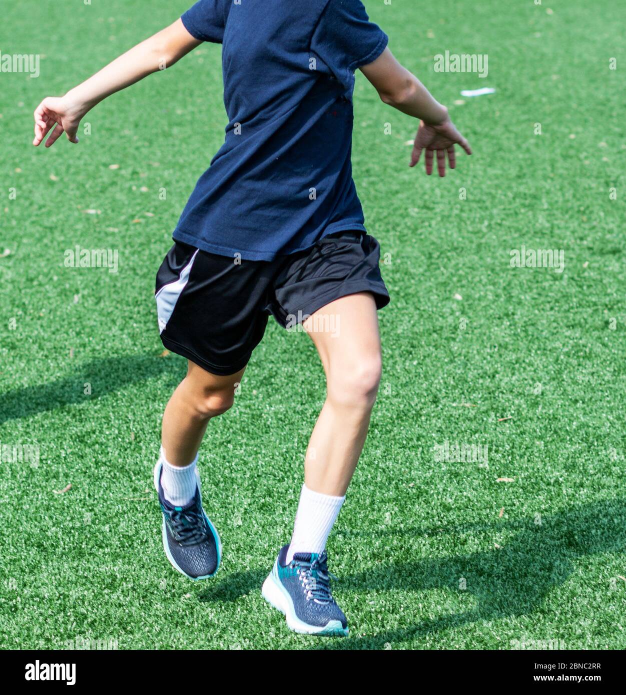 A young high school athlete is performing kereoke bounding drill while warming up on a turf field during sports team practice. Stock Photo