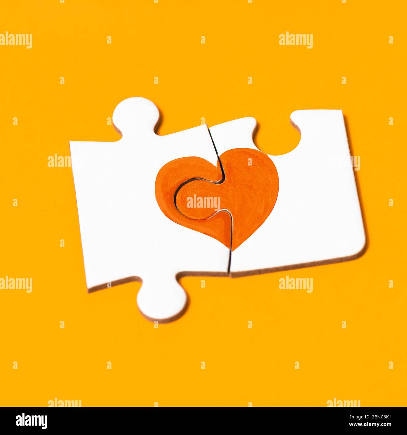 closeup of two pieces of a puzzle forming an orange heart, in support of people affected by multiple sclerosis, on an orange background Stock Photo
