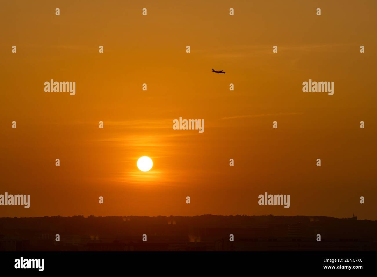 Seting sun with an airplane silhouette in colourful sky background Stock Photo