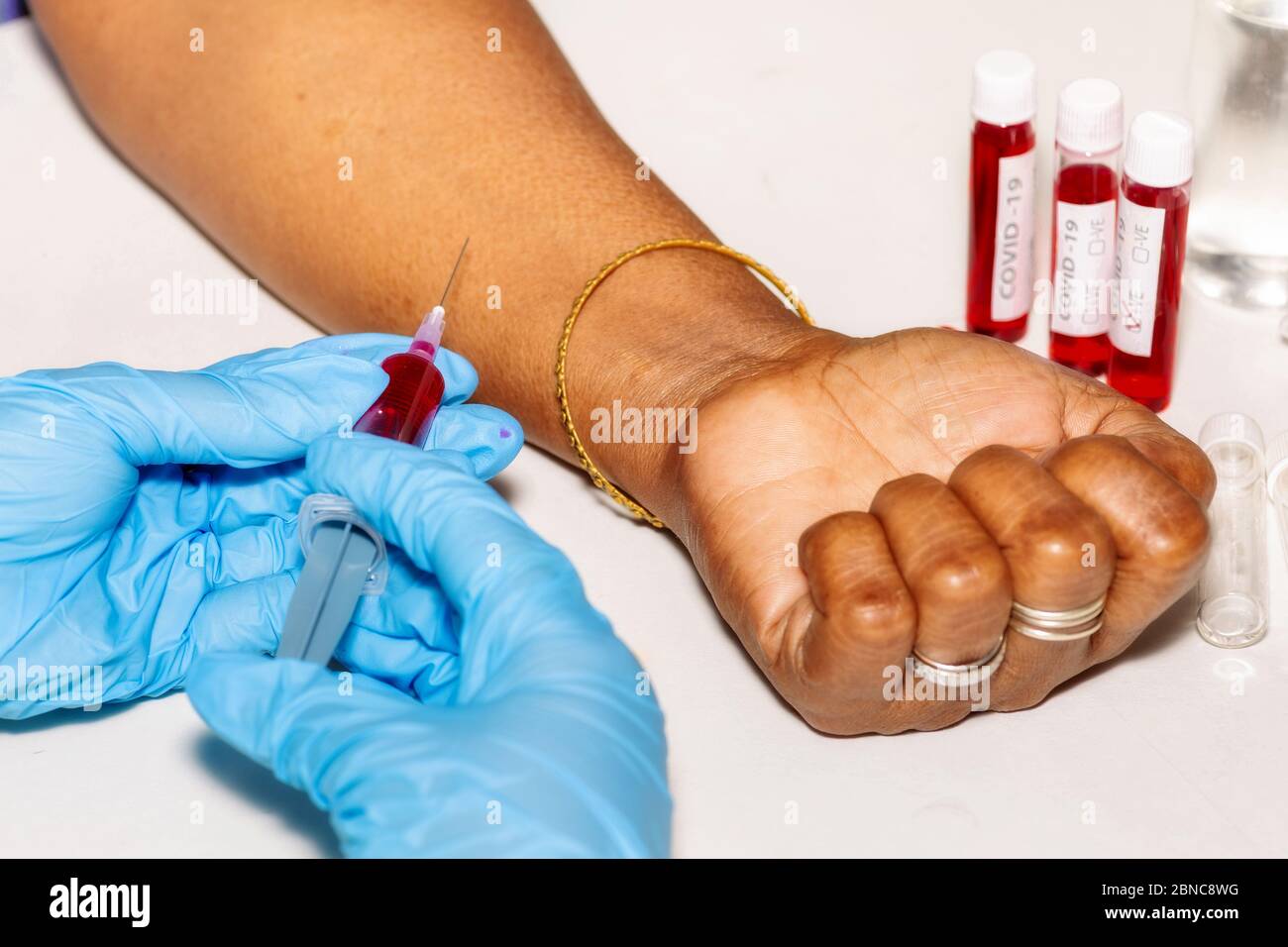 Hands of a medical worker holding an injection syringe with blood sample taken from an Indian woman patient for coronavirus test Stock Photo