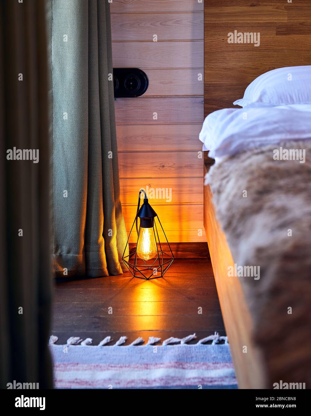 Modern interior of cozy bedroom in the hotel with glowing loft lamp on the wooden floor Stock Photo