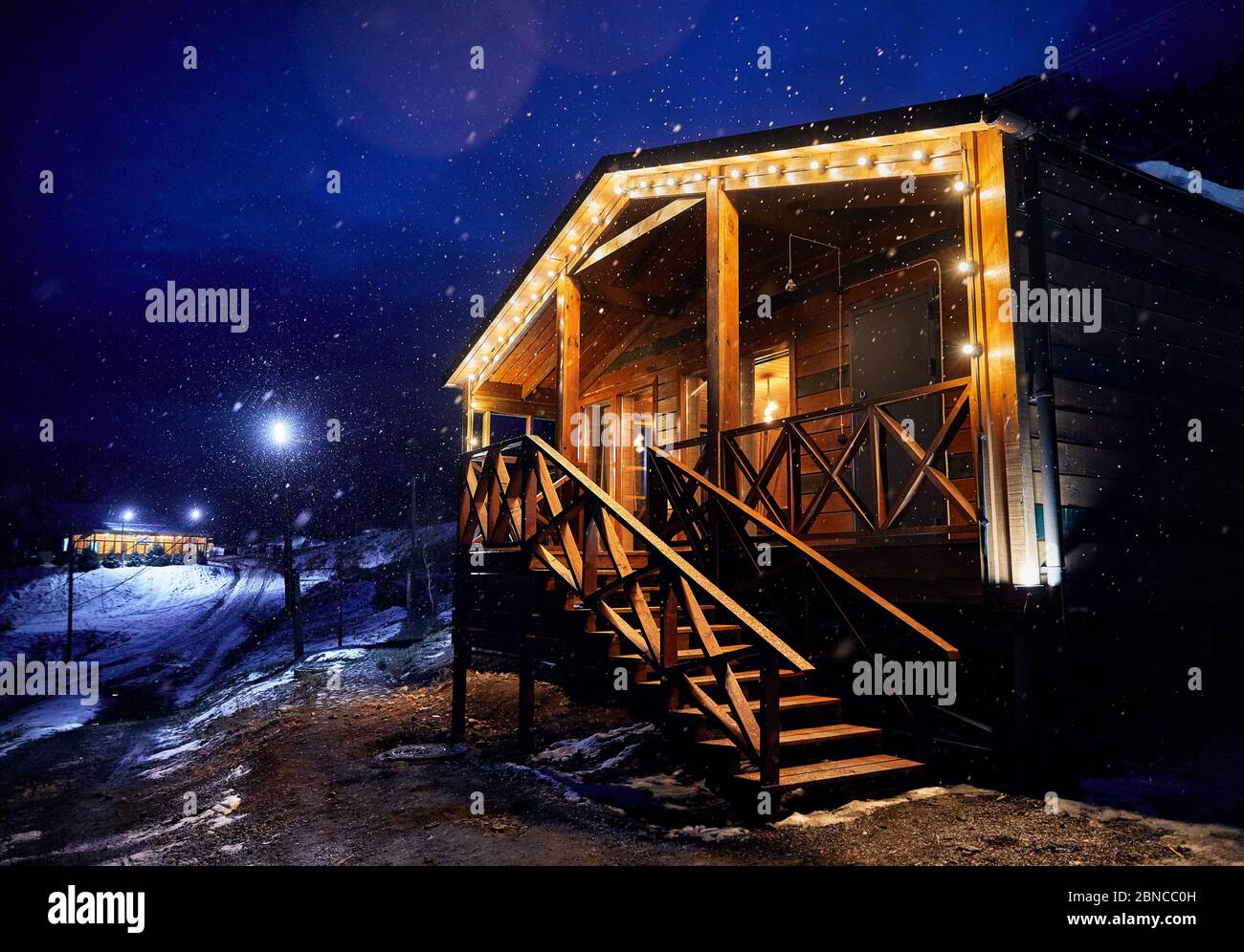Modern wooden house decorated with yellow glowing bulbs in snowfall at the mountain resort Stock Photo