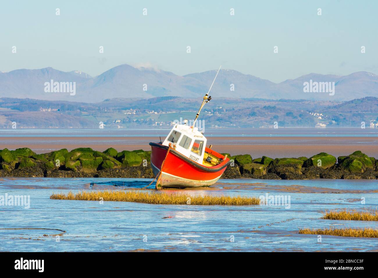 Fishing boat at low tide, Morecambe, with the Coniston Fells in the Lake District behind Stock Photo