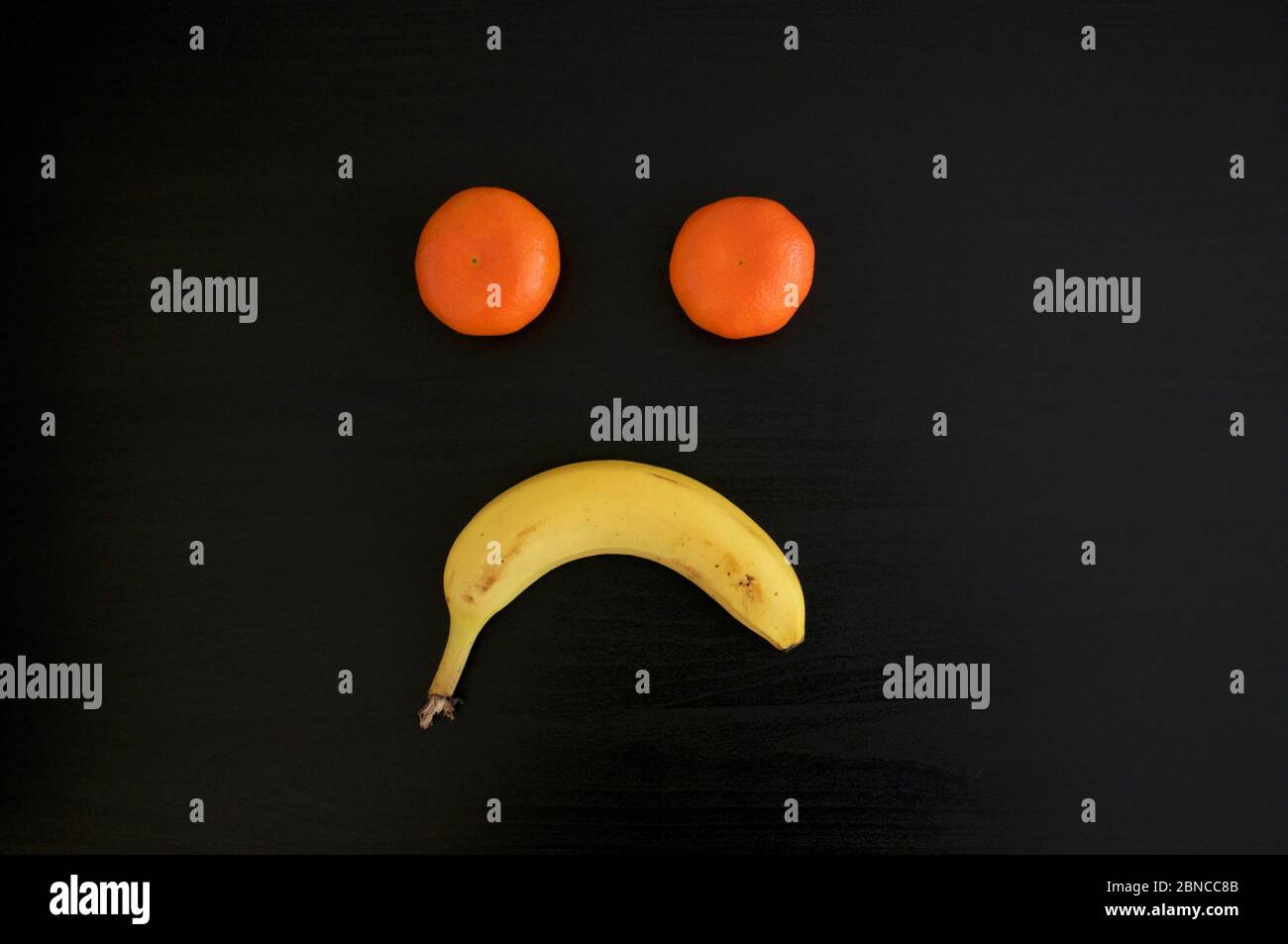 A sad grimace made out of tangerines and a banana on black background.This can be used for conceptual photo as sadness, depression, and negativity Stock Photo