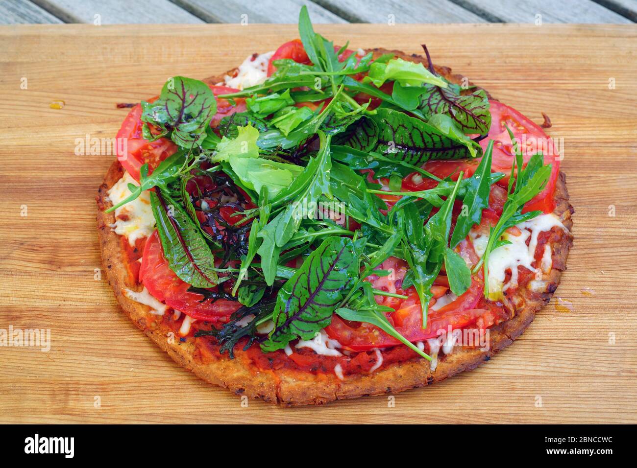 A pizza with red sauce and fresh salad on a gluten-free cauliflower crust Stock Photo