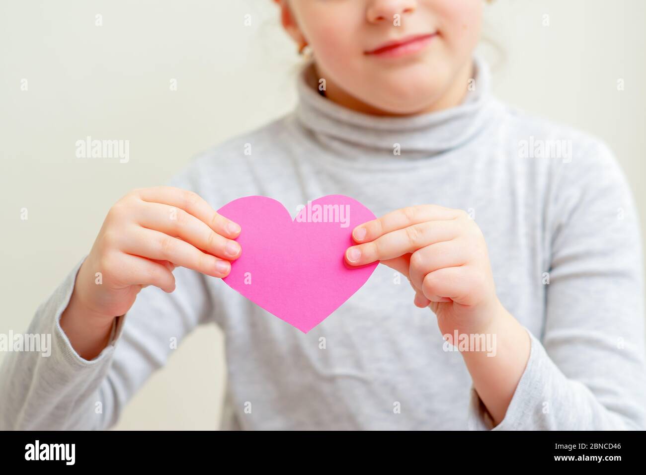 Child is holding pink paper heart standing on white background. Child love concept. Stock Photo