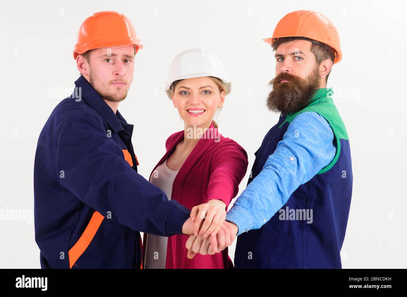 team work concept - two young men and woman in builders uniform and ...