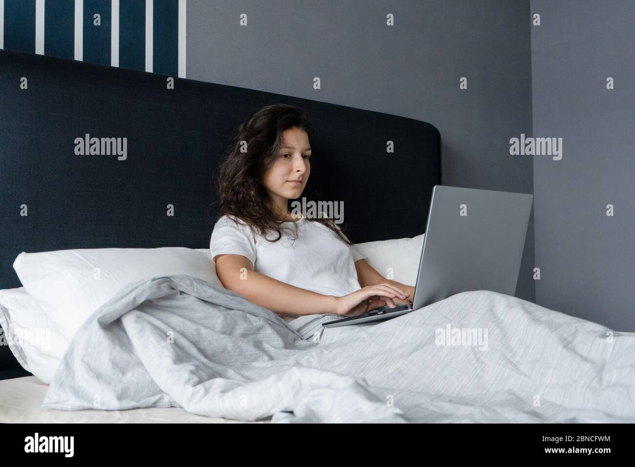 Beautiful brunette girl in bed with a laptop. Work from morning to late night. Electronic gadgets before bedtime or in the morning Stock Photo