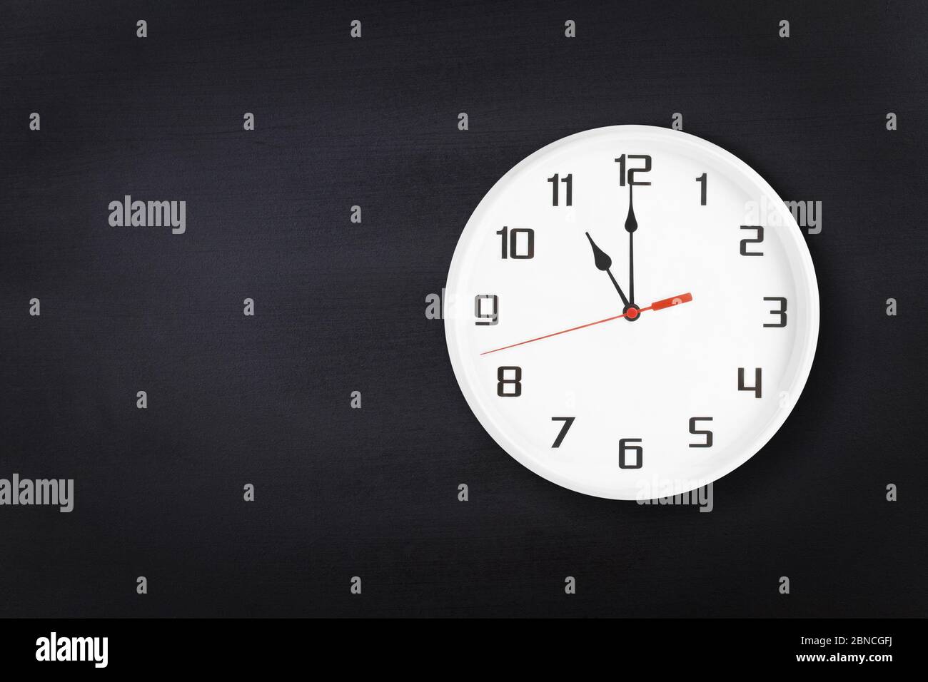 White wall clock on black chalkboard background. 11 a.m. or 11 p.m. Stock Photo