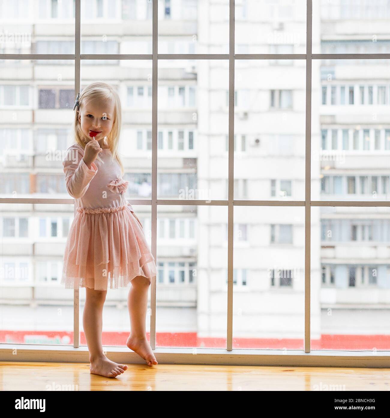 Portrait of pretty 3 years old girl wearing pink dress eating lollipop Stock Photo