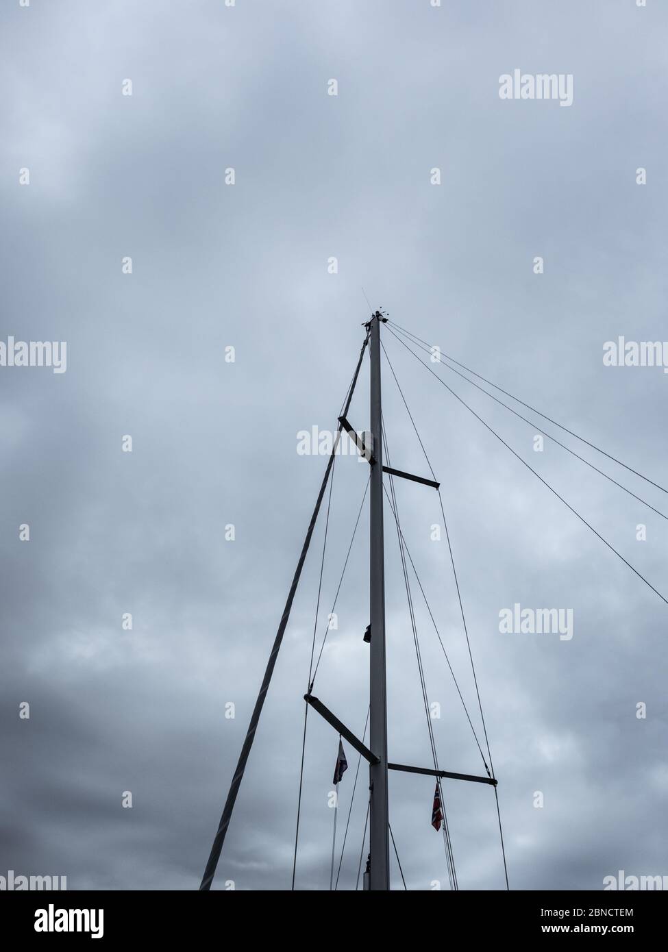 Sailing ship mast on heavy dark grey cloudy stormy sky background. Vertical close-up view Stock Photo