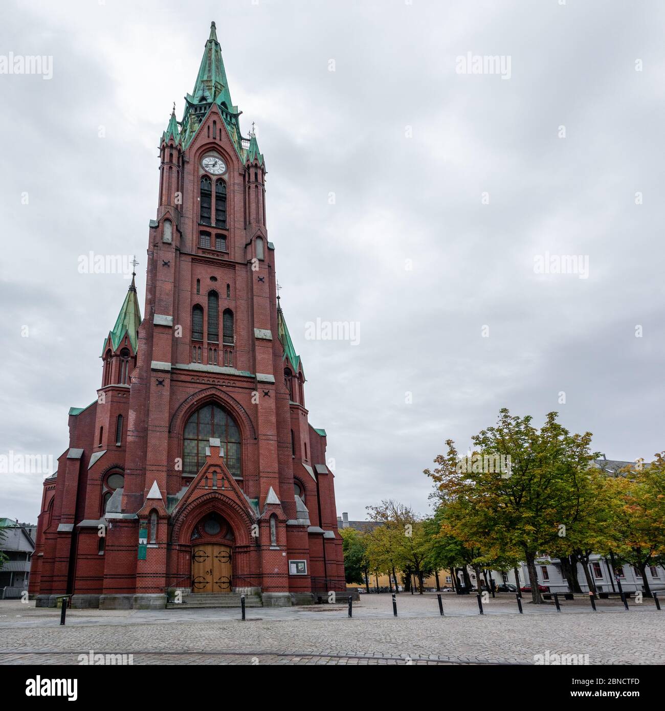 Panoramic view of high St. John's Church (Johanneskirken) in Bergen, Norway. Gothic-revival church with red brick & copper details. Cloudy autumn day Stock Photo