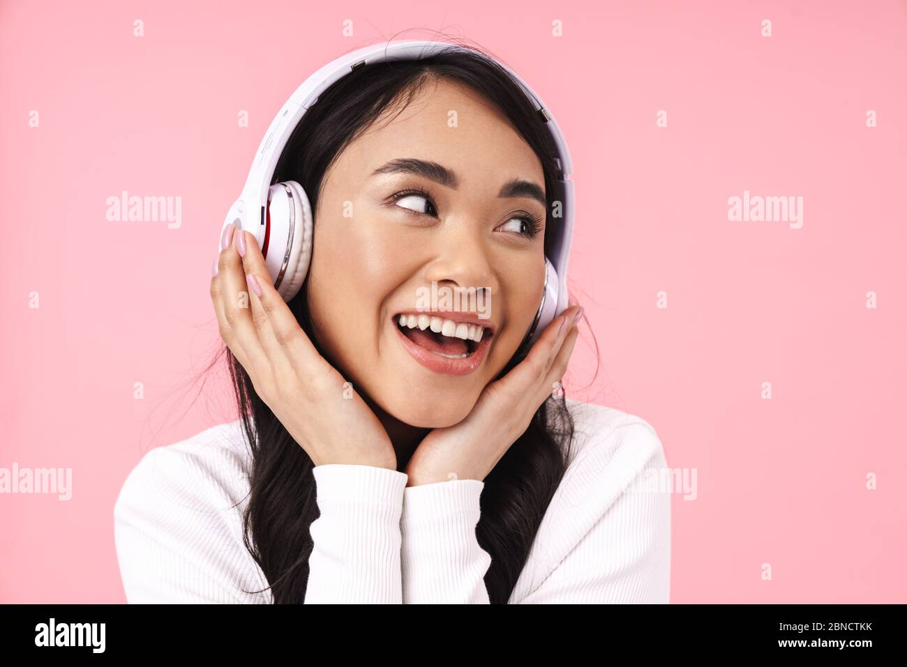 Cheerful pretty young asian woman listening to music with wireless ...
