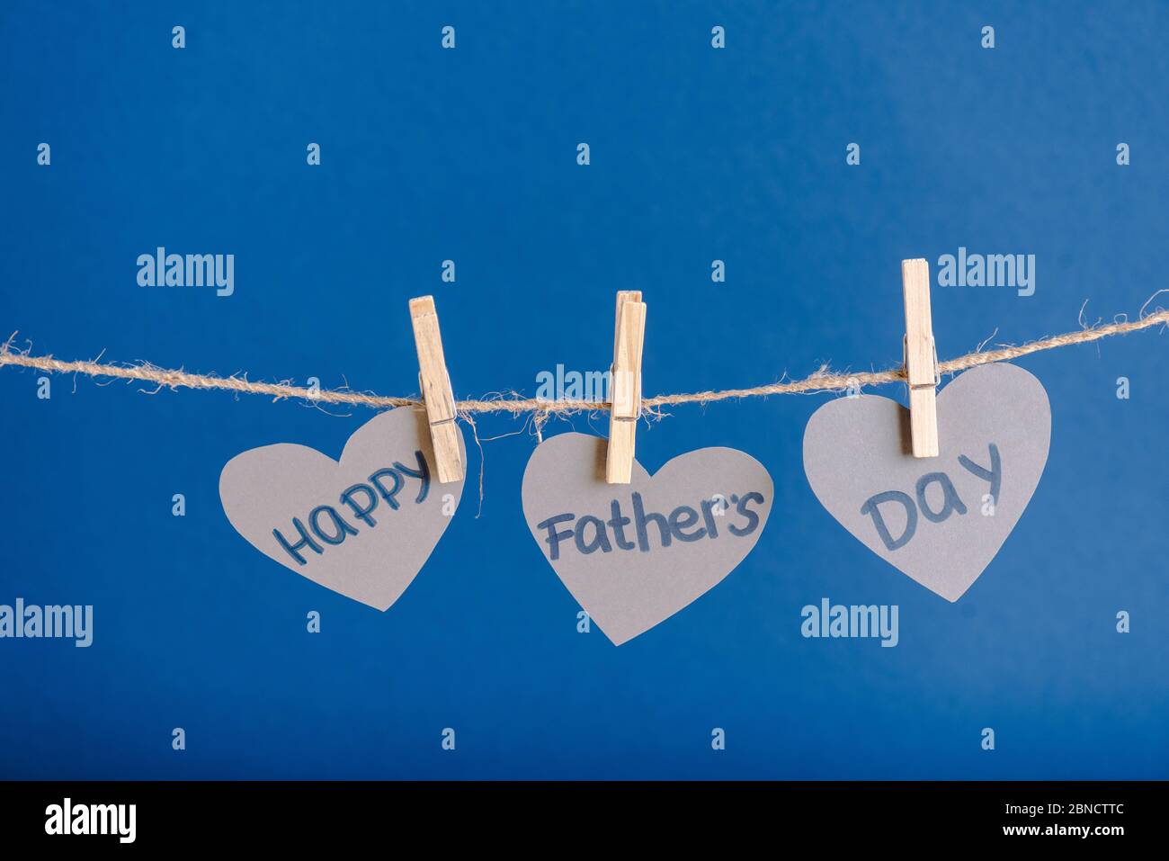 Grey heart-shaped greeting cards hanging on rope with clothespins isolated on blue Stock Photo