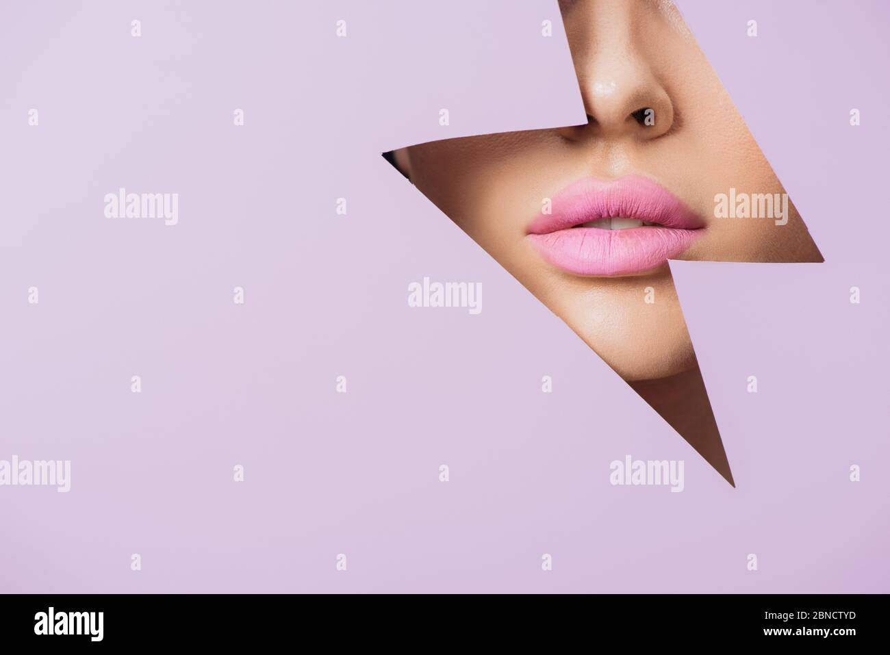 Cropped view of female face with pink lips in hole in violet paper ...