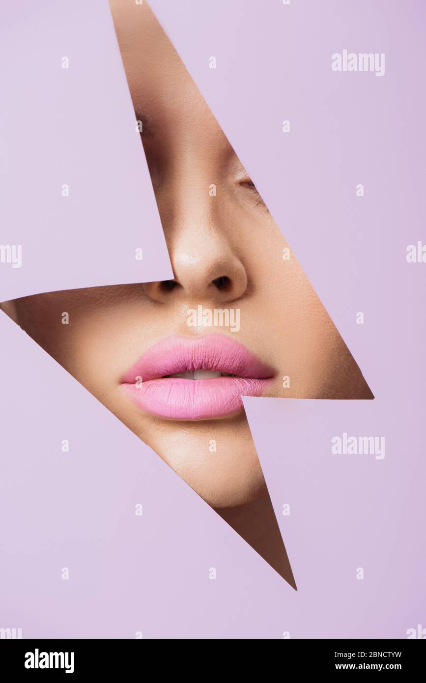 Cropped view of female face with pink lips in hole in violet paper ...