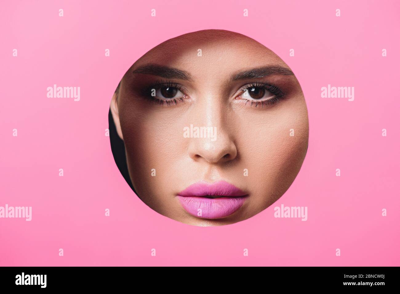 Woman with smoky eyes and pink lips looking at camera across hole in paper Stock Photo